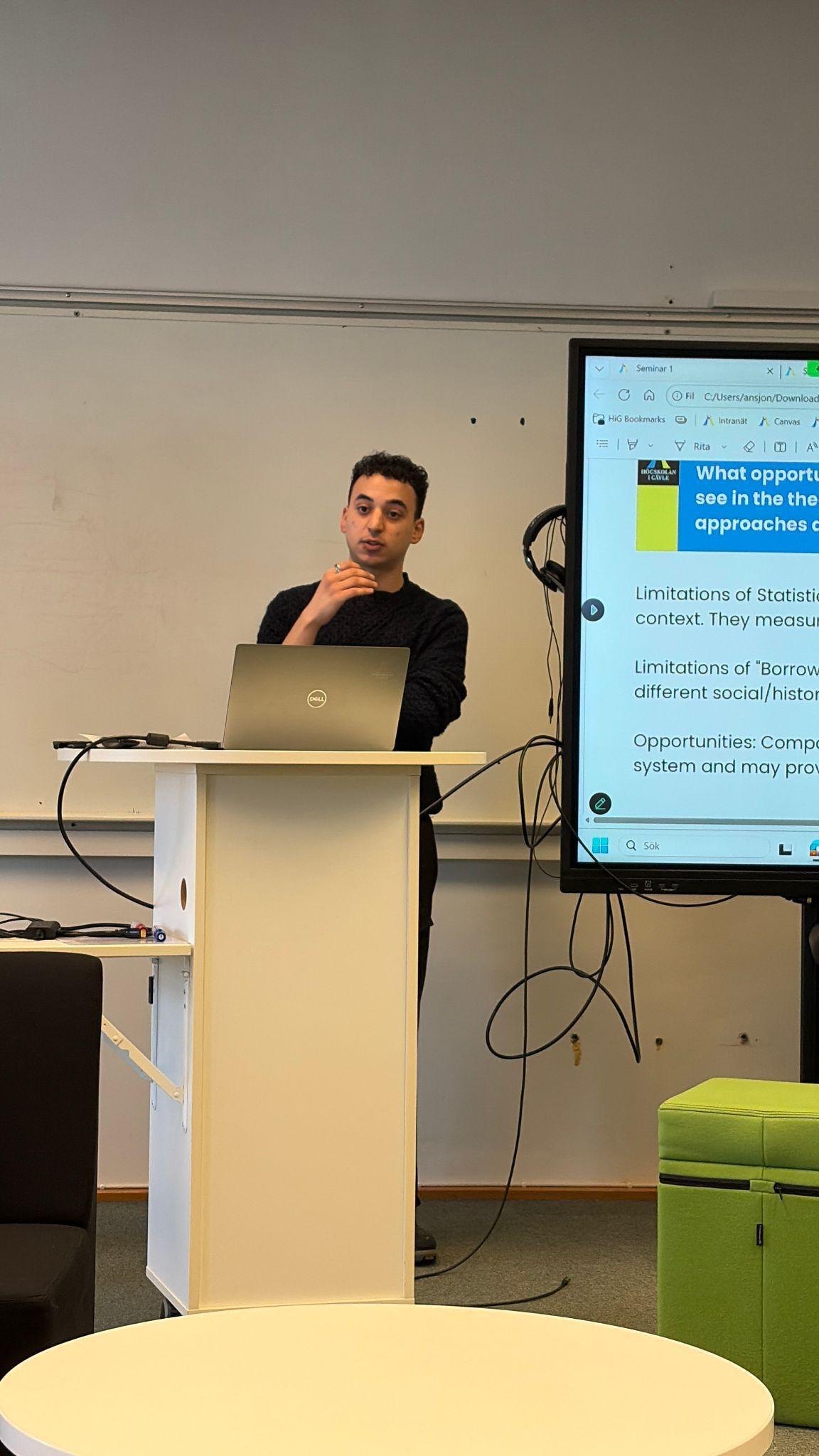 Youssef Farouk presenting at a lectern next to a screen with slides