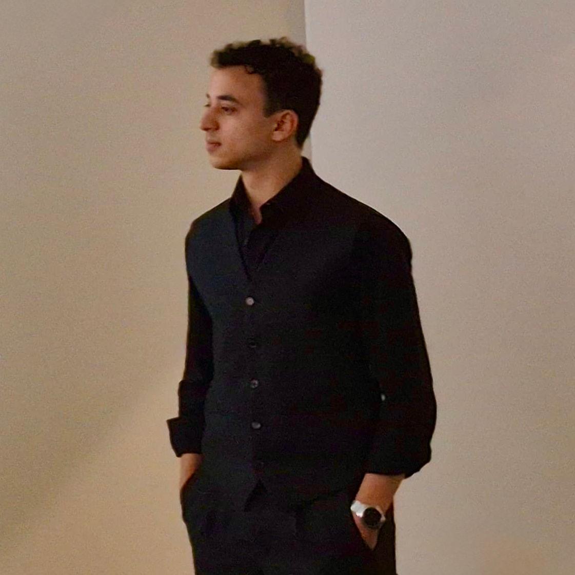 Youssef Farouk in a dark shirt and waistcoat, looking to the side